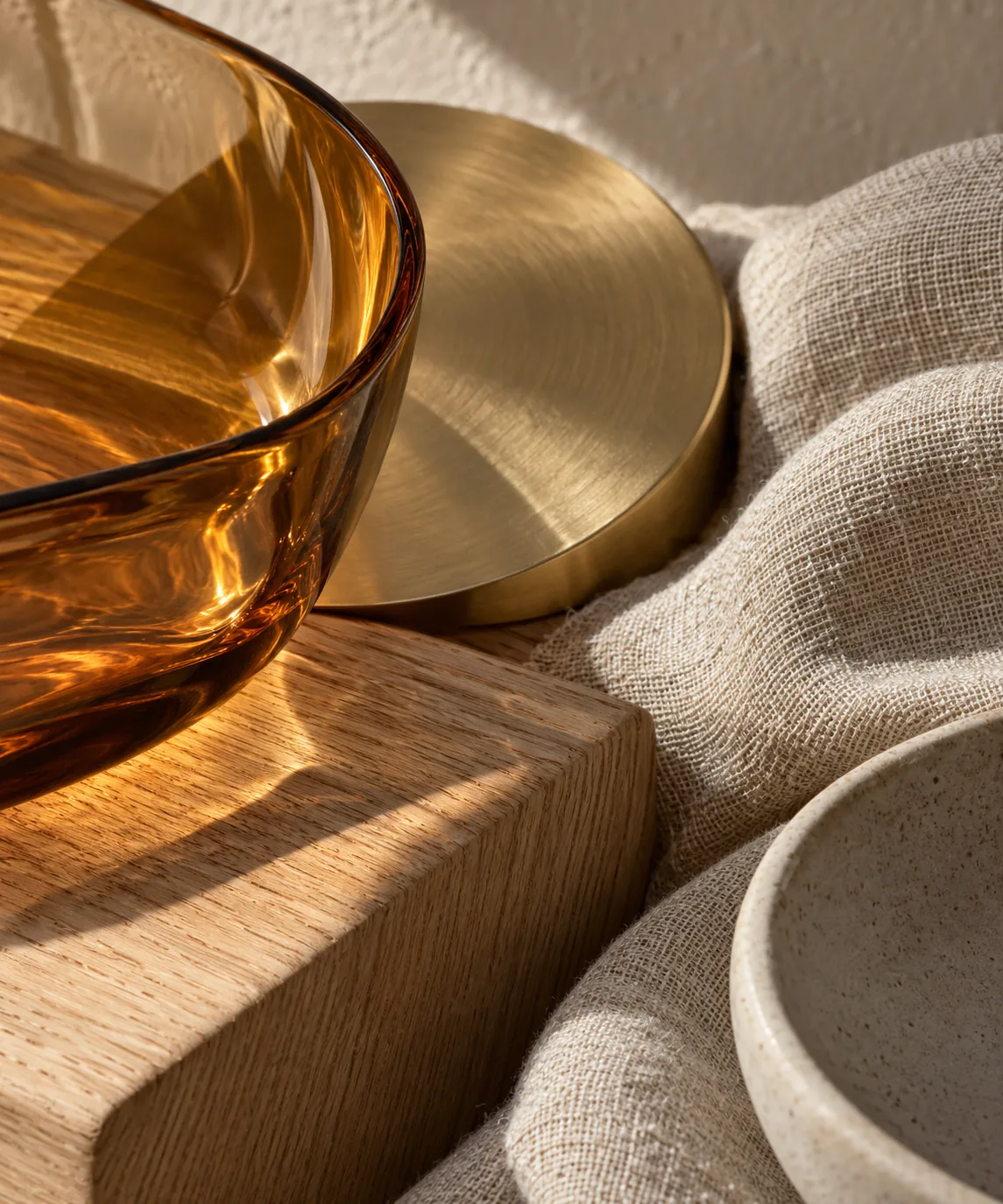 Close view of amber glass, brushed brass, oak, and linen